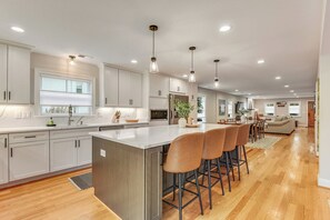 A modern kitchen with white cabinets, a large island with bar stools, and pendant lighting.