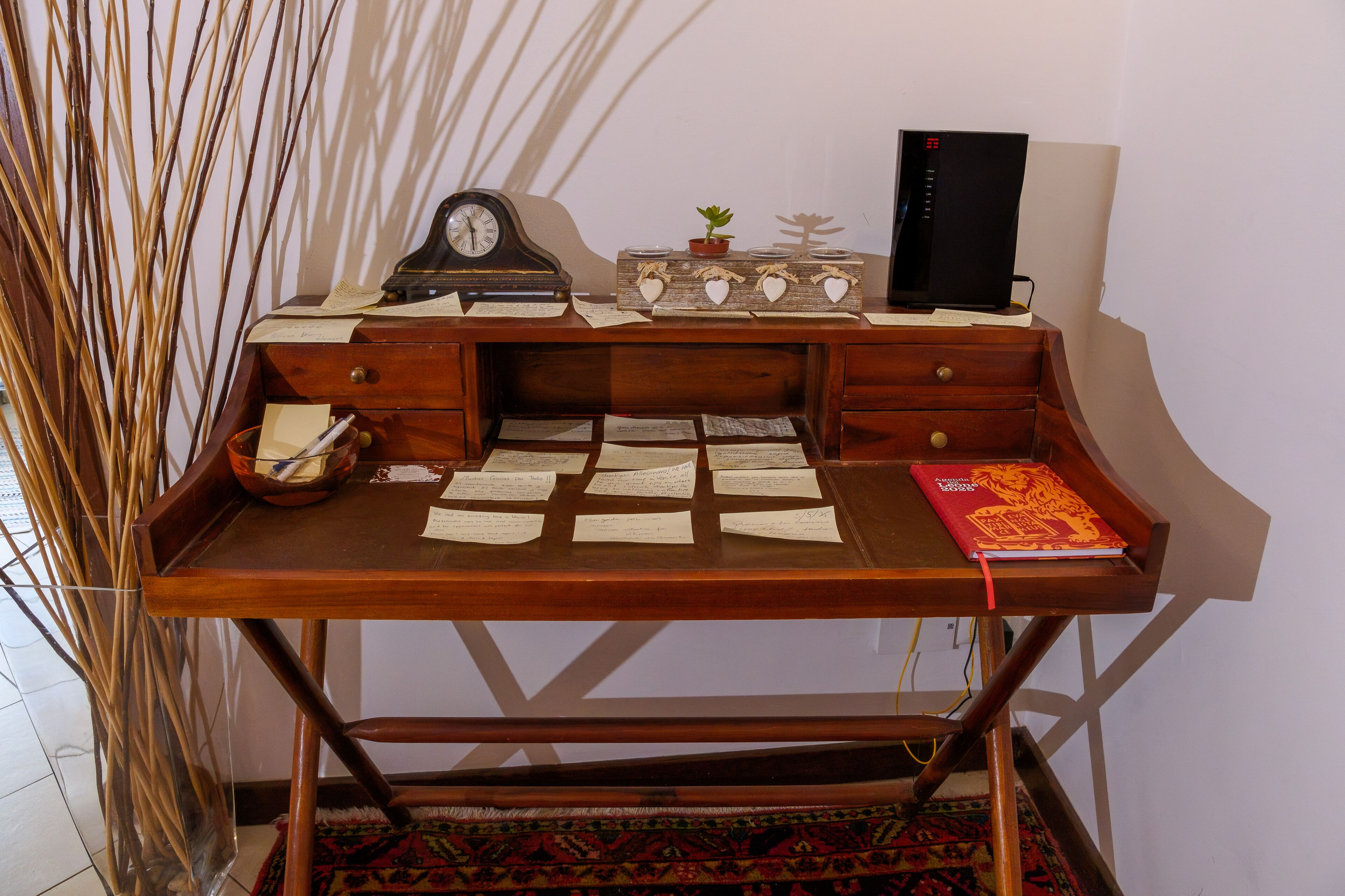 Un bureau en bois avec des papiers, une horloge, une petite plante et un livre.
