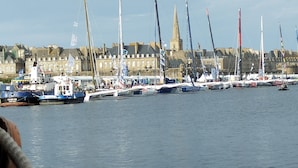 Ein Hafen mit mehreren vor Anker liegenden Segelbooten, im Hintergrund ein markanter Kirchturm und Gebäude entlang der Uferlinie.