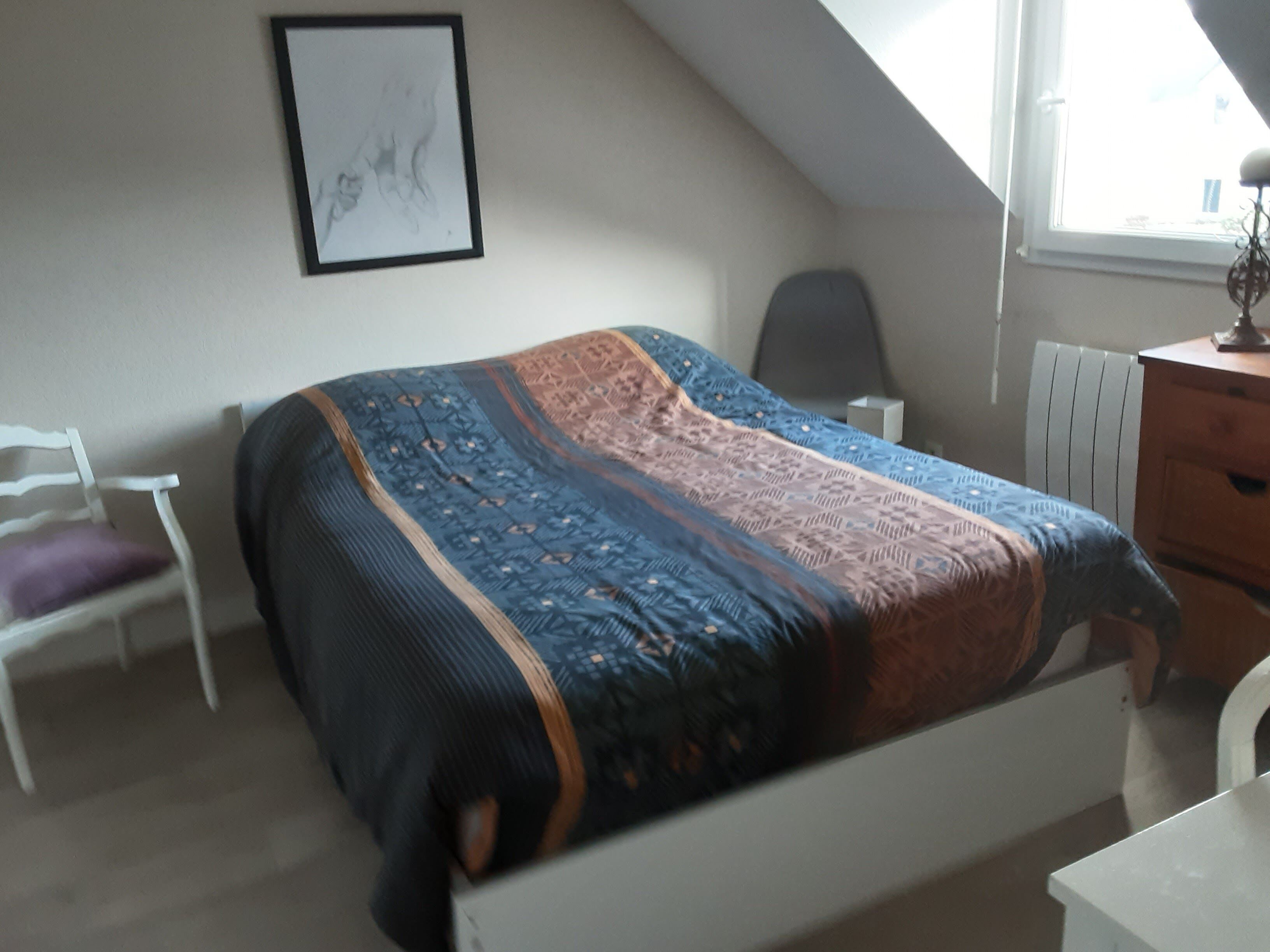 A bedroom with a bed, a chair, a desk, and a radiator.