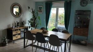 Ein Essbereich mit einem Holztisch und Stühlen, einem Spiegel, einer Zimmerpflanze und Blick durch ein mit Vorhängen drapiertes Fenster.