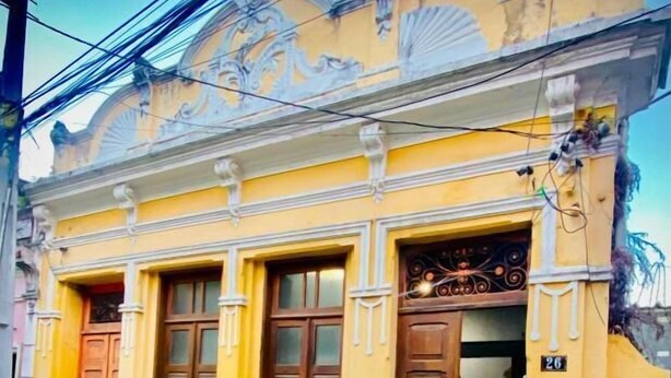 Un edificio amarillo con detalles arquitectónicos ornamentales, incluyendo molduras decorativas y un amplio ventanal en arco.