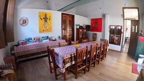 Un comedor con una larga mesa de madera, sillas y un banco. Hay cuadros en las paredes y una puerta con una pintura roja.