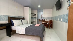 Habitación de hotel compacta con cama, escritorio, silla, una mesita y televisor montado en la pared.