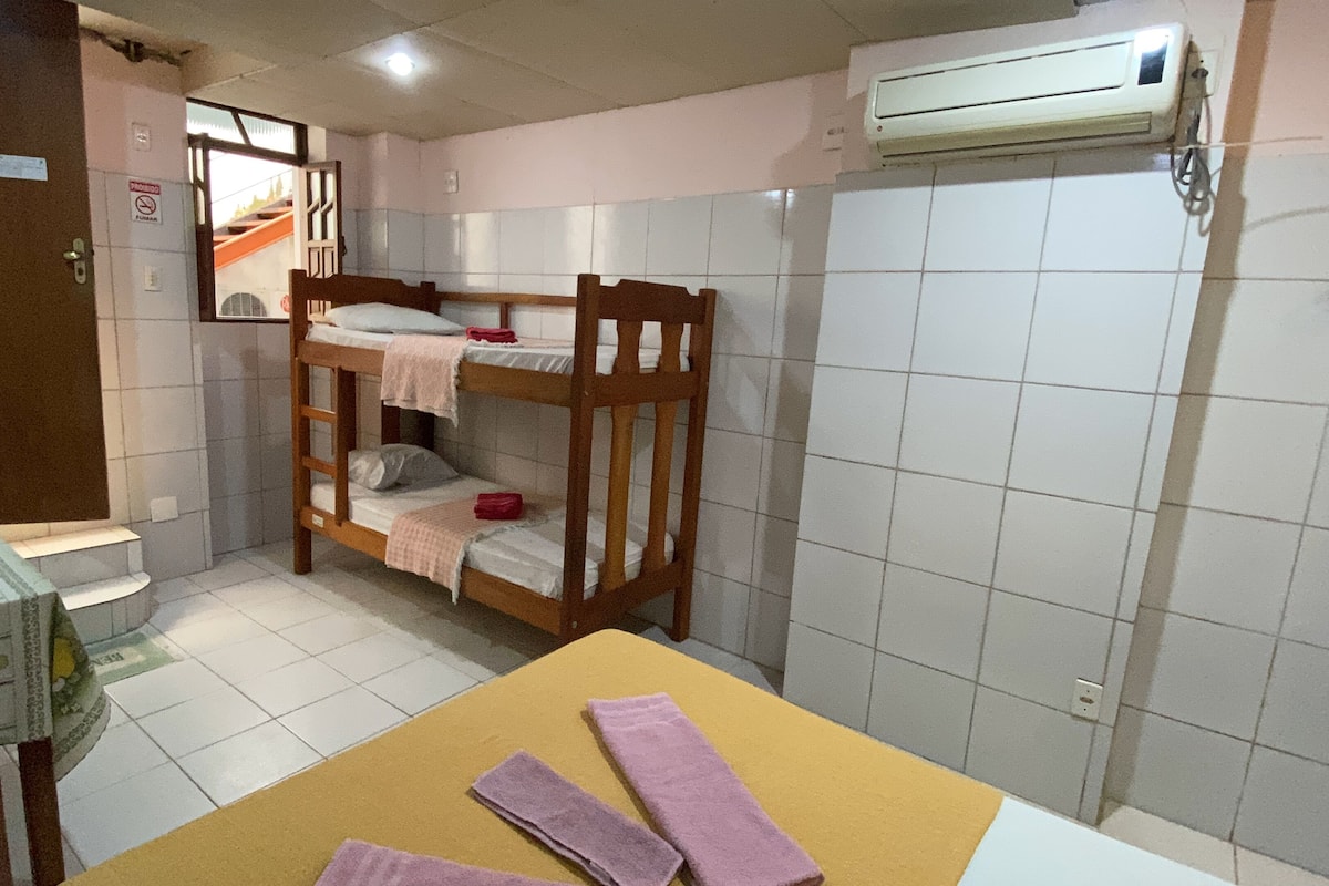 A small, compact room with bunk beds, a table with towels, and an air conditioning unit on the wall.