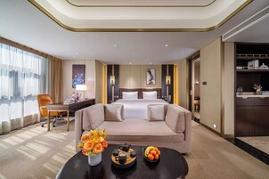 Una habitación de hotel con cama, sofá, escritorio y una mesa de centro con flores y fruta.