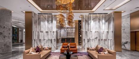 A spacious lobby with a central seating area, marble walls, and a modern chandelier.