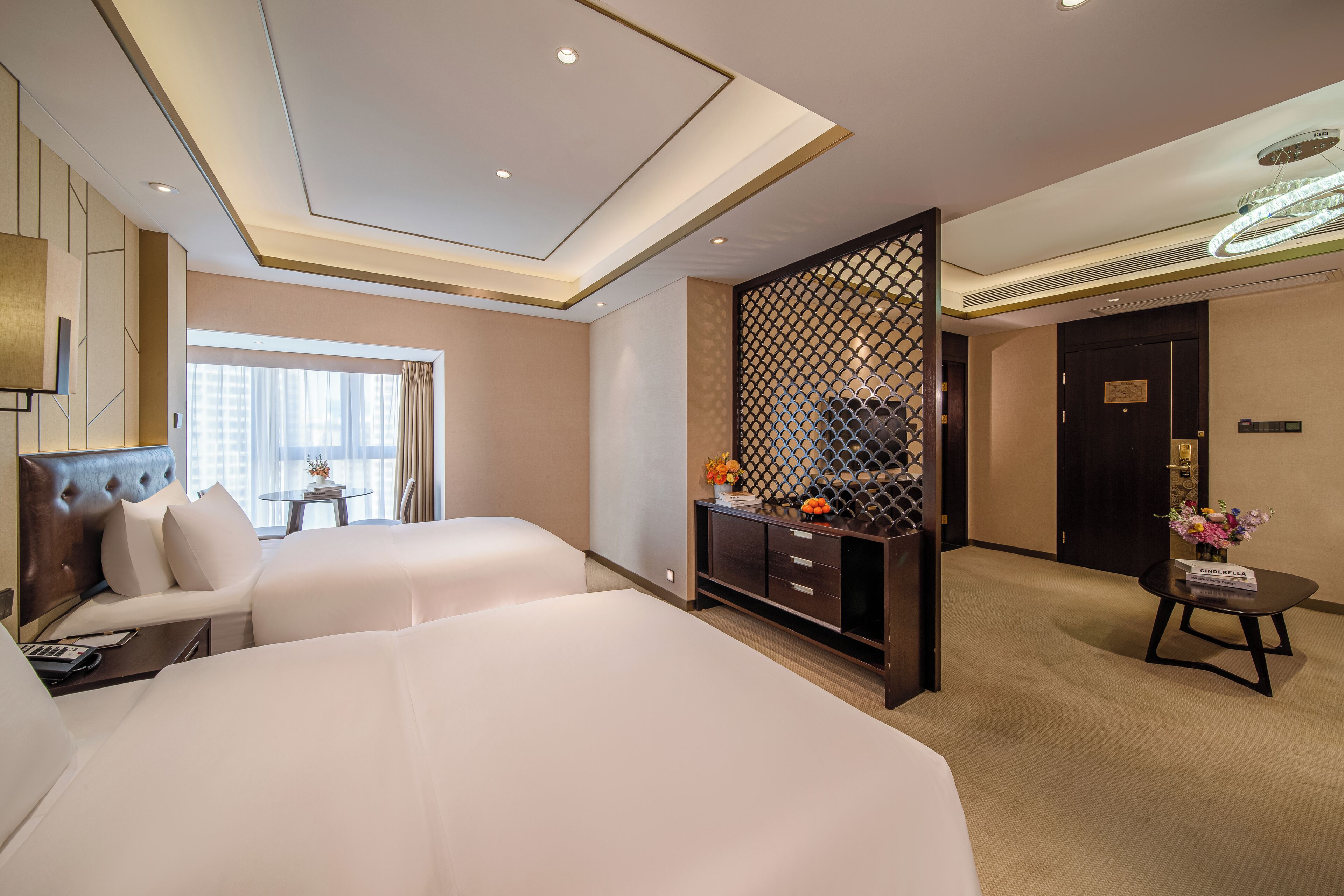 Habitación de hotel con dos camas, un escritorio, una silla, un separador decorativo y vistas de la ciudad.