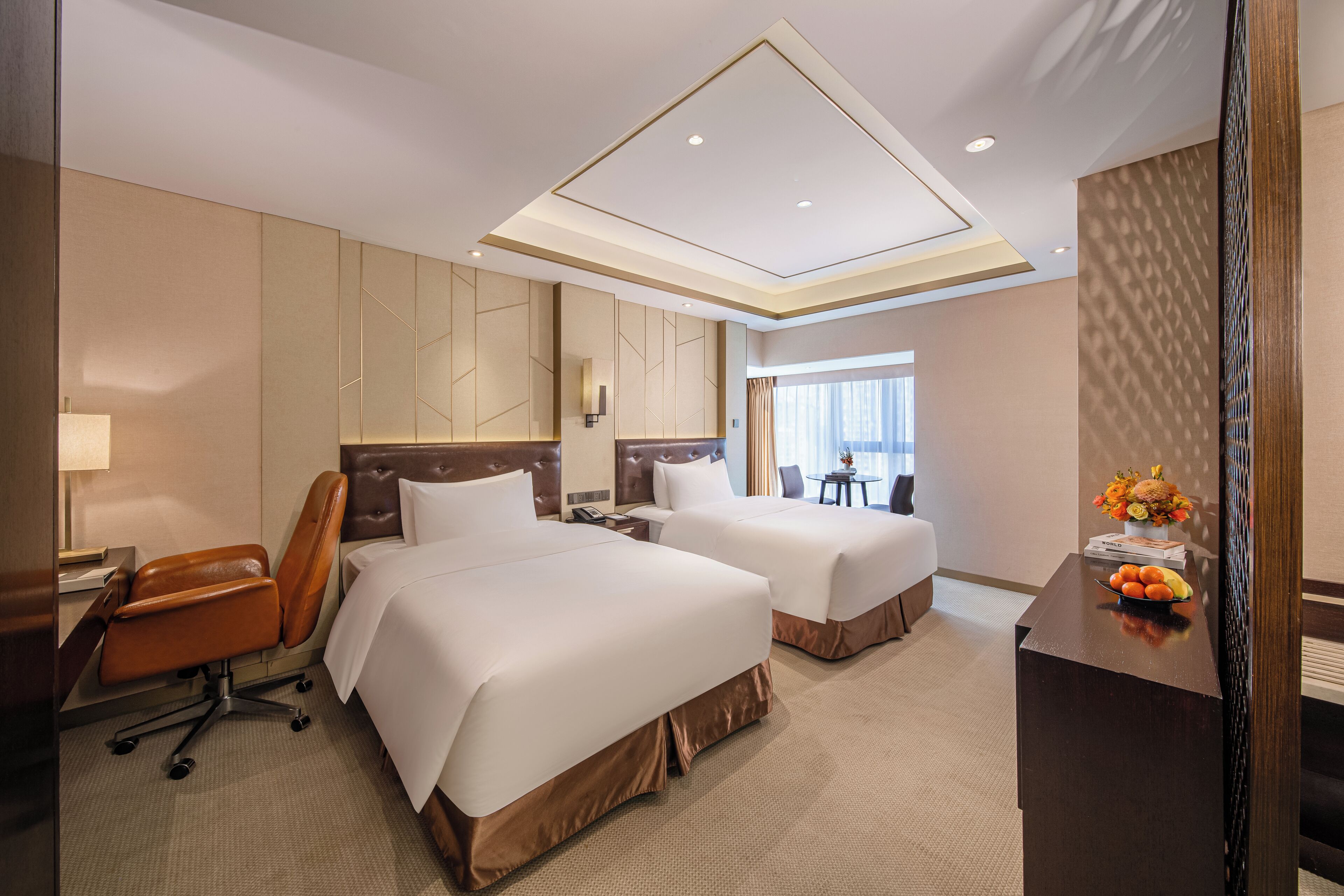 Een hotelkamer met twee bedden, een bureau, een stoel en een tafeltje met fruit.