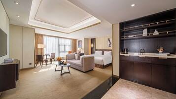 A modern hotel room with a large bed, a sofa, a dining area, and a kitchen counter.