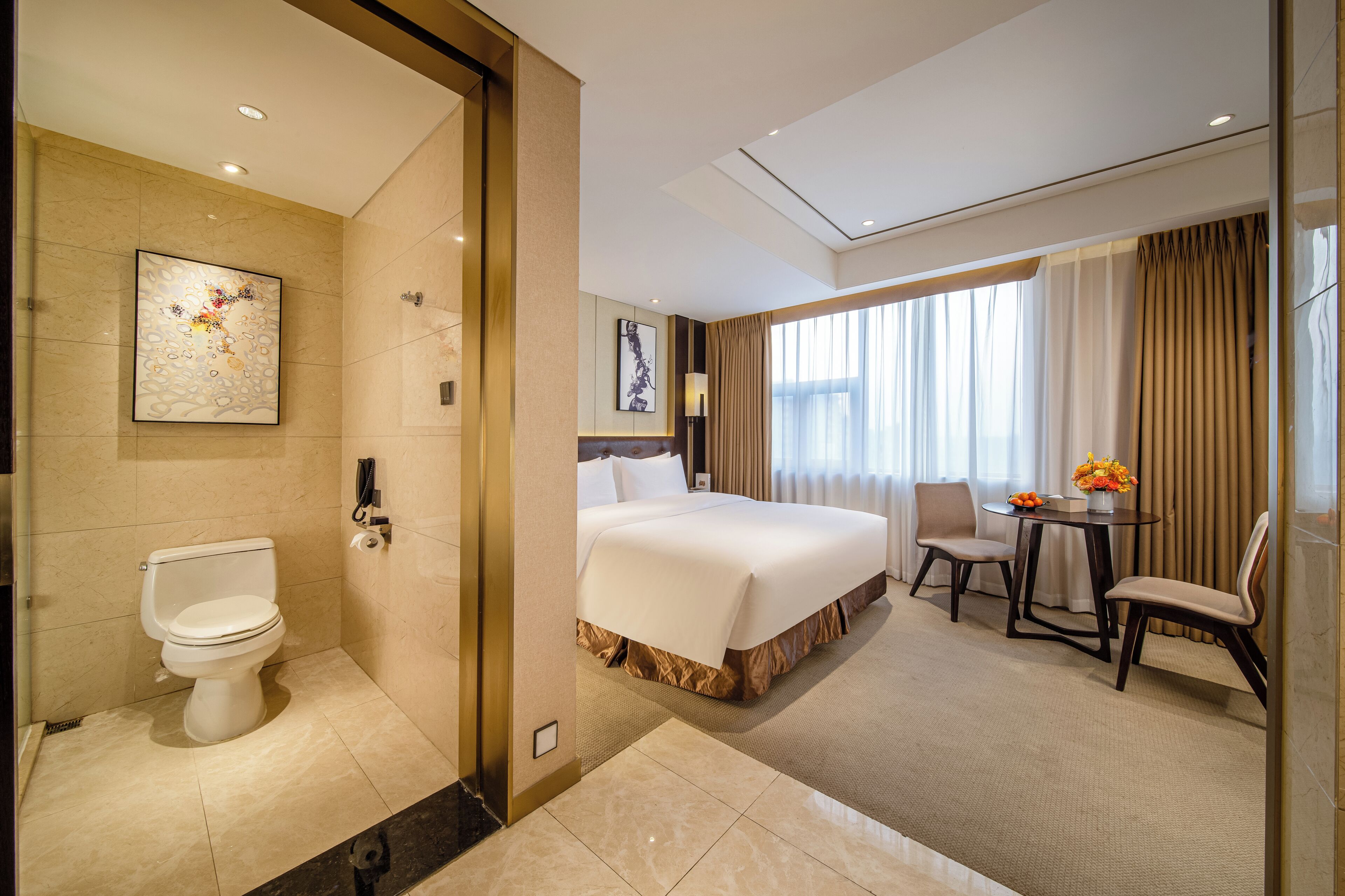 Habitación de hotel con cama, escritorio con silla, baño con inodoro y un cuadro en la pared.