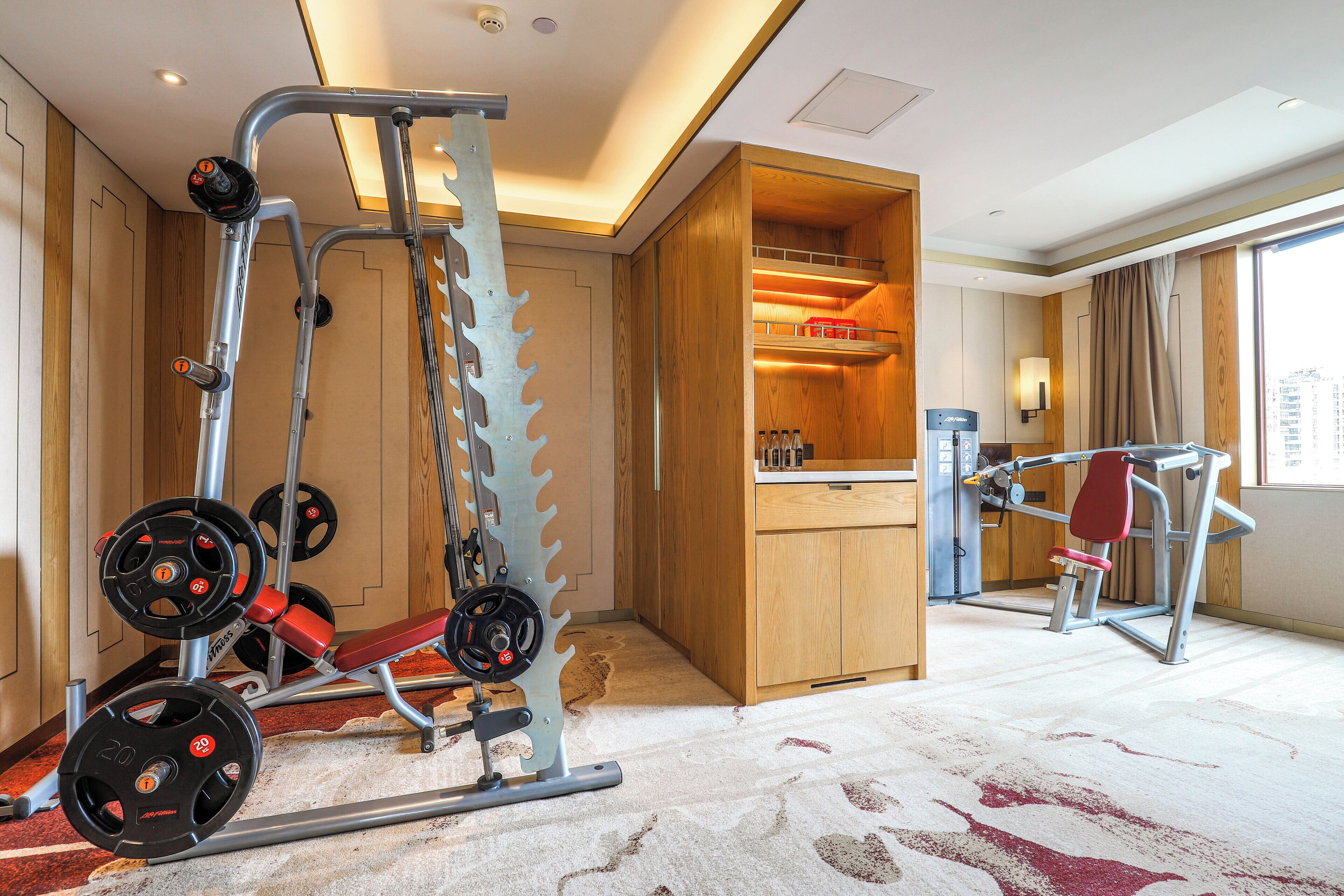 A hotel room with a gym area including a weight bench, a squat rack, and a bench press.