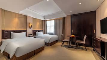 A hotel room with two beds, a desk, a chair, a TV, and a large window with curtains.