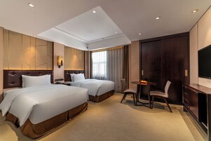 Habitación de hotel con dos camas, un escritorio, una silla, un televisor y un ventanal con cortinas.