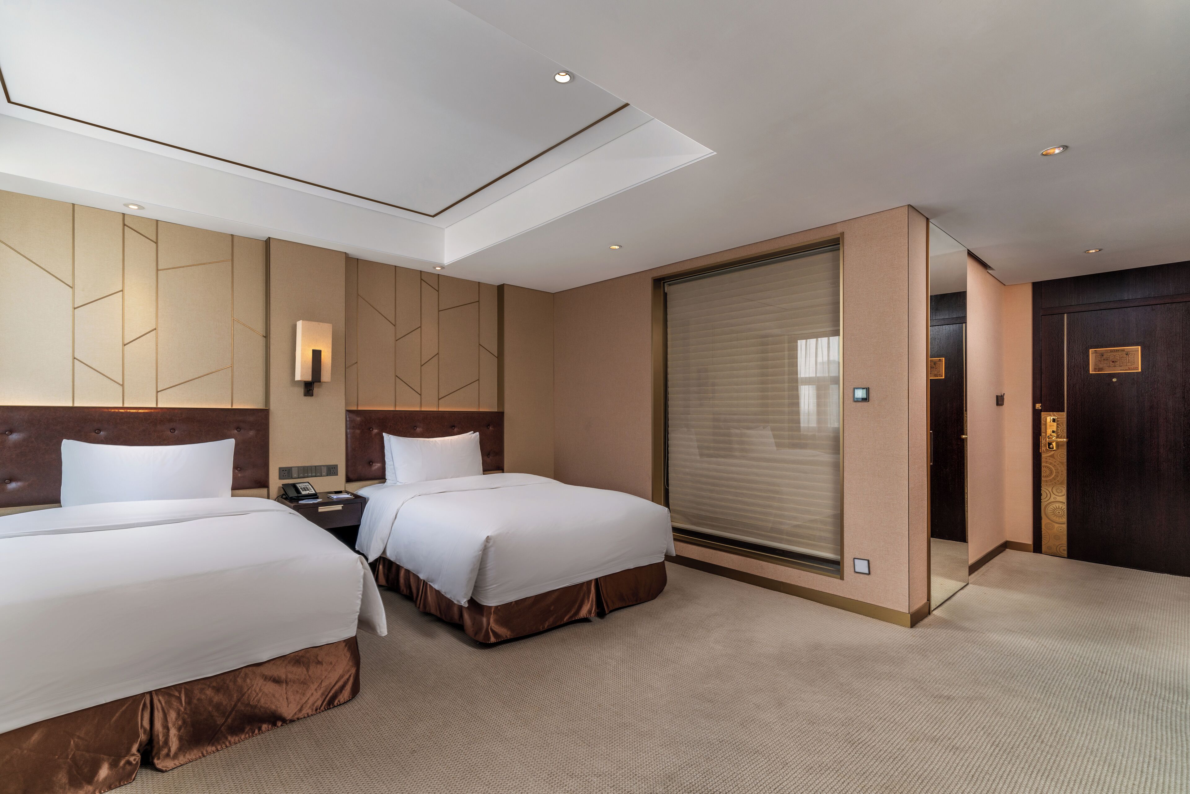 A hotel room with two beds, a large sliding door, and a modern ceiling design.