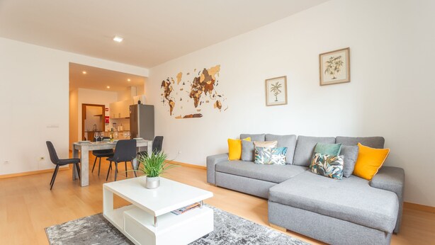A modern living room with a grey sofa, a coffee table, and a dining area with chairs and a table.