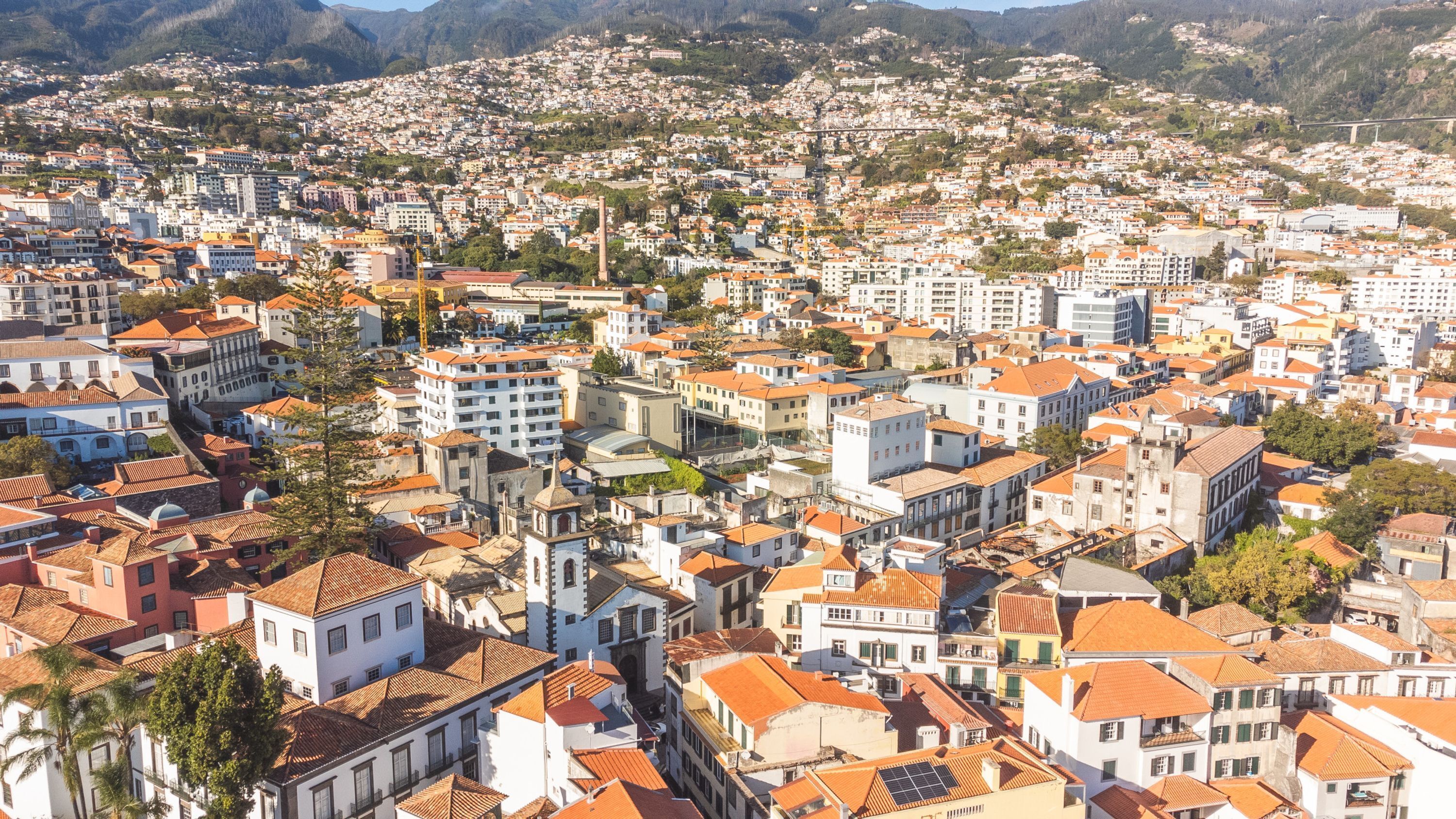 Une zone urbaine densément peuplée, où se côtoient des immeubles résidentiels et commerciaux, et qui se distingue par la diversité de ses styles architecturaux et la présence d’un pont imposant en arrière-plan.