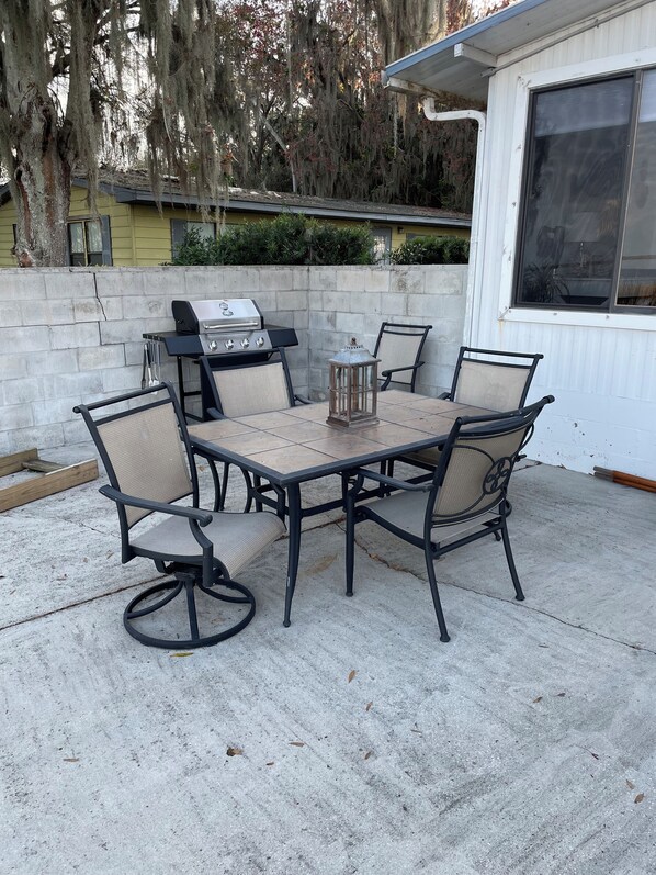 An outdoor patio with a grill, a table, and four chairs.