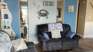Una sala de estar con un sofá gris oscuro, un tapete a rayas, y una pared decorada con una figura de cangrejo y la palabra "OCEAN".