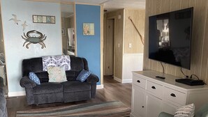 Una sala de estar con un sofá gris oscuro, un sillón verde claro, un tapete a rayas, un televisor y un aparador de madera.