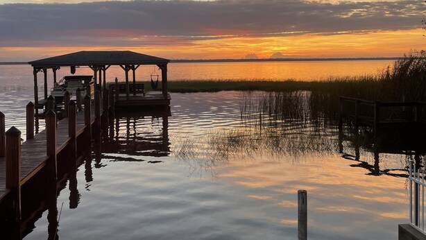 Un muelle se adentra en aguas tranquilas con un atardecer de fondo.