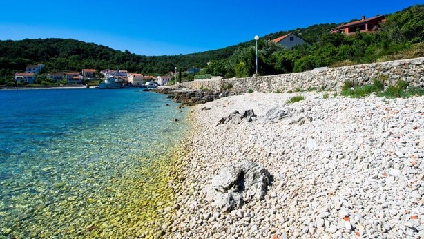 A pebble beach with clear water, houses on a hillside, and a stone wall. - A relaxing beachside house with a hot tub overlooking the sea in Zadar County. (Zadar County)
