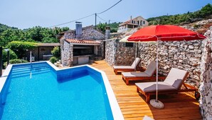 A swimming pool with lounge chairs and a red umbrella, surrounded by stone walls and a wooden deck. - A relaxing beachside house with a hot tub overlooking the sea in Zadar County. (Zadar County)