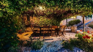An outdoor seating area with a stone table and benches, surrounded by lush greenery and a stone wall. - A relaxing beachside house with a hot tub overlooking the sea in Zadar County. (Zadar County)