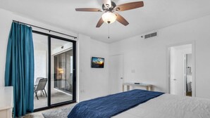 Ein Schlafzimmer mit einem Bett, einem Deckenventilator, einer Schiebetür und einem kleinen Tisch.