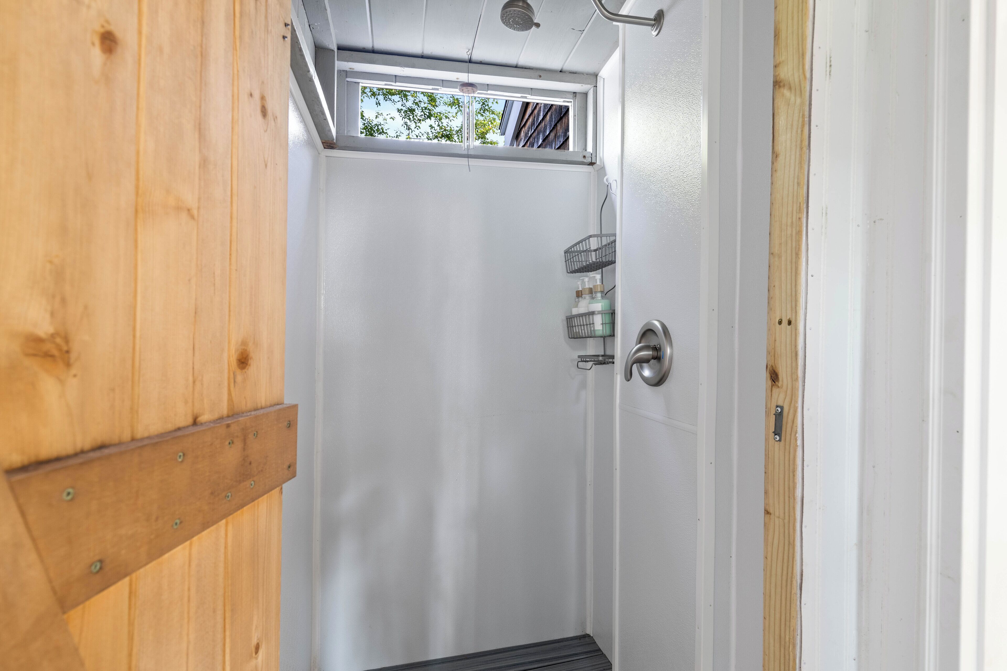 Une salle de bain avec une douche, une fenêtre et une porte en bois.