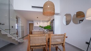 A modern dining area with wicker chairs, a glass staircase, and a kitchen in the background. - Exclusive Penthouse With Picuzzi Steps From Beach (Punta Cana)