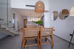 A modern dining area with wicker chairs, a glass staircase, and a kitchen in the background. - Exclusive Penthouse With Picuzzi Steps From Beach (Punta Cana)