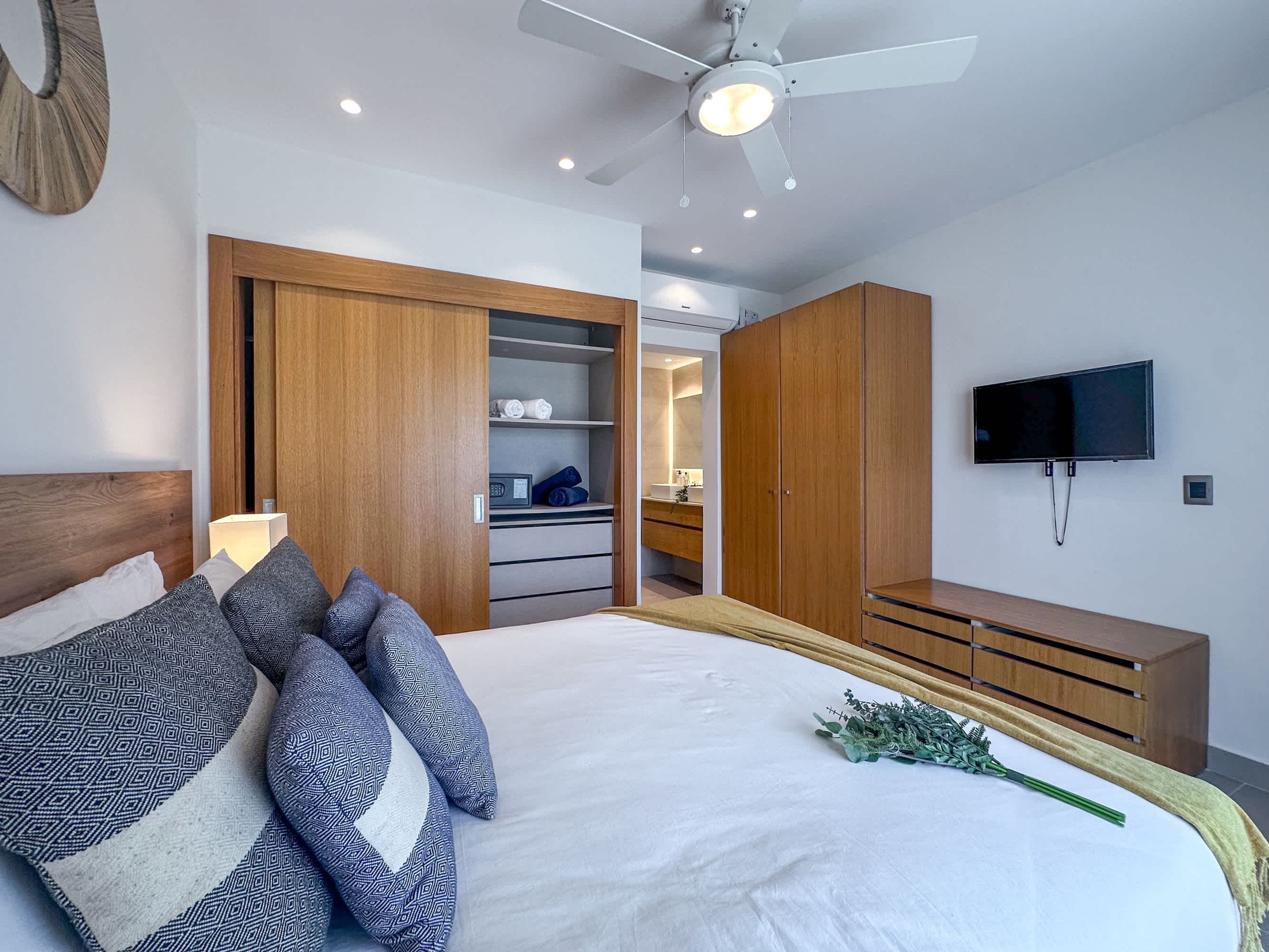 A modern bedroom with a bed, wooden wardrobe, built-in TV, and a ceiling fan.