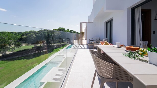 A modern balcony with a glass railing overlooking a swimming pool and lush greenery. - Exclusive Penthouse With Picuzzi Steps From Beach (Punta Cana)