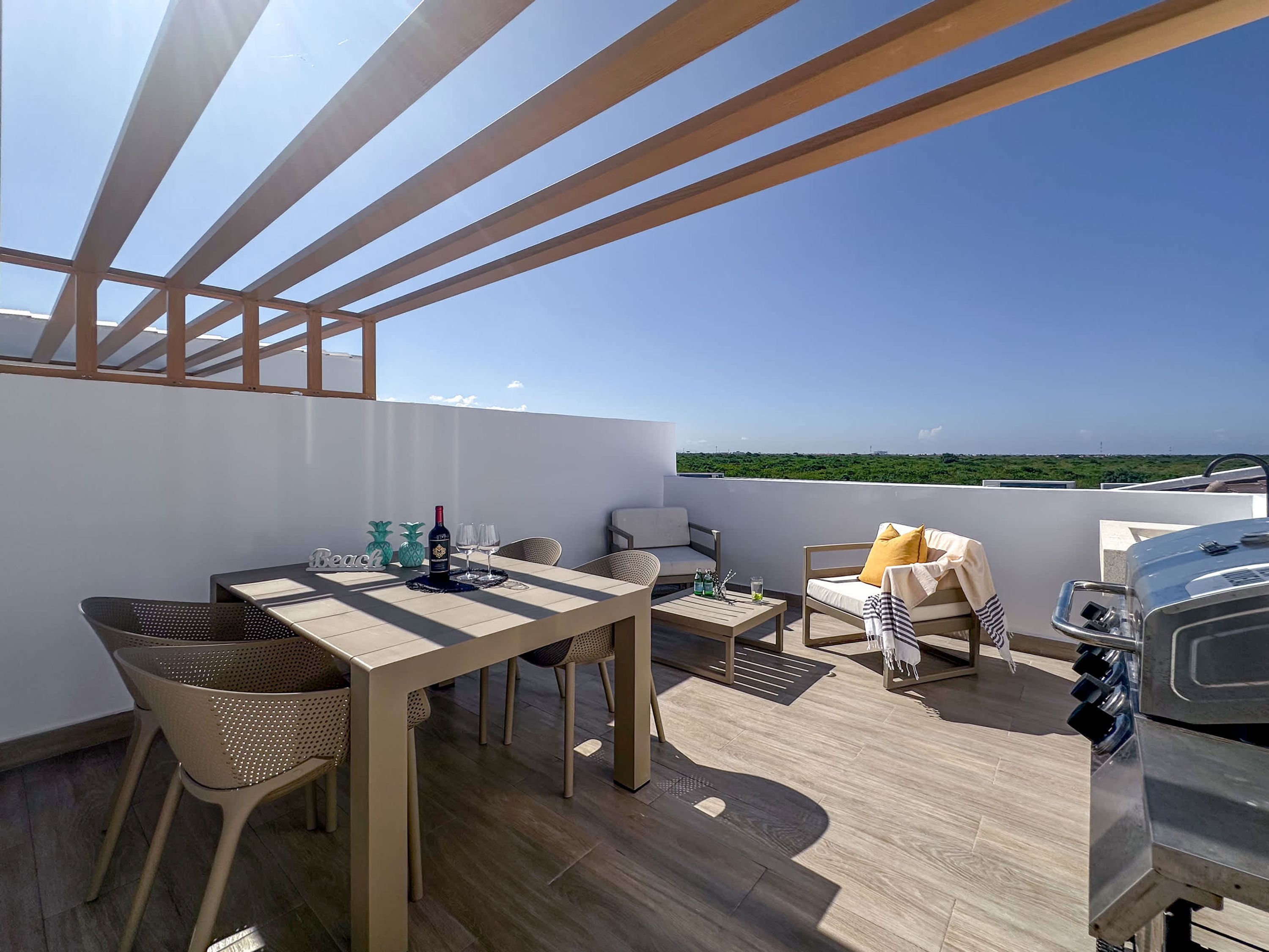 A rooftop terrace with a table, chairs, a grill, and a view of the landscape.