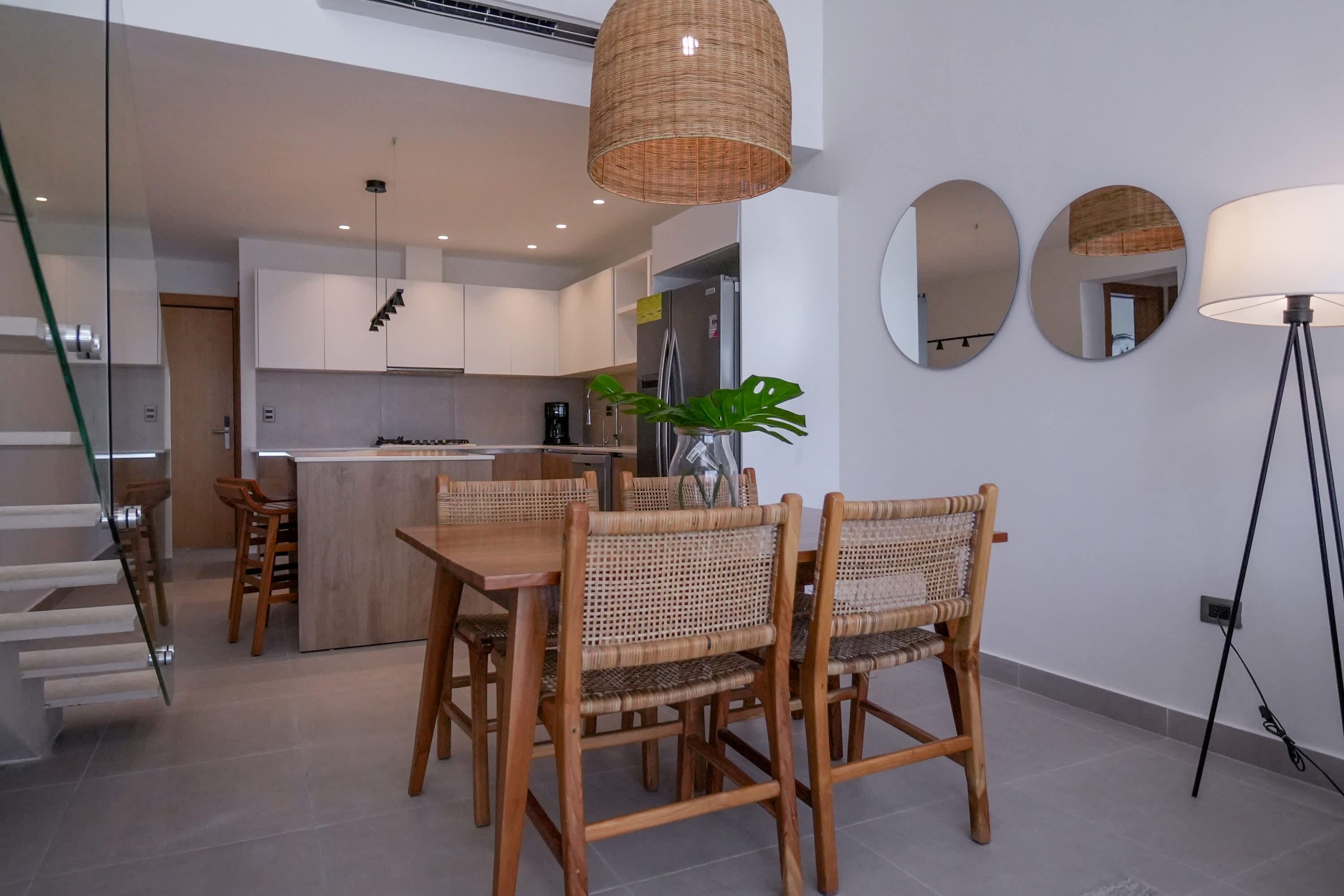 A modern kitchen with white cabinets, a central island, and a dining area with wicker chairs.