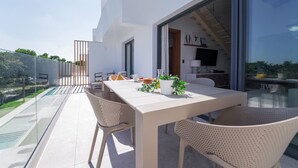 A modern outdoor dining area with a white table and wicker chairs, overlooking a swimming pool and greenery. - Exclusive Penthouse With Picuzzi Steps From Beach (Punta Cana)