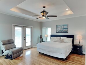 A bedroom with a bed, a ceiling fan, a chair, a nightstand, and a painting on the wall.