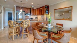 A modern kitchen with wooden cabinets, a stainless steel refrigerator, and a glass dining table with chairs. - Oceanfront Seaside Sanctuary Stunning Views w 2 Lanais Whales Watching Haven (Lahaina)