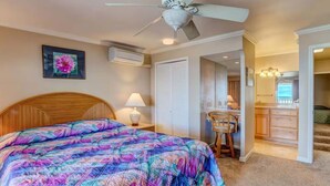 A bedroom with a bed, a ceiling fan, a nightstand with a lamp, and a door leading to a bathroom. - Oceanfront Seaside Sanctuary Stunning Views w 2 Lanais Whales Watching Haven (Lahaina)