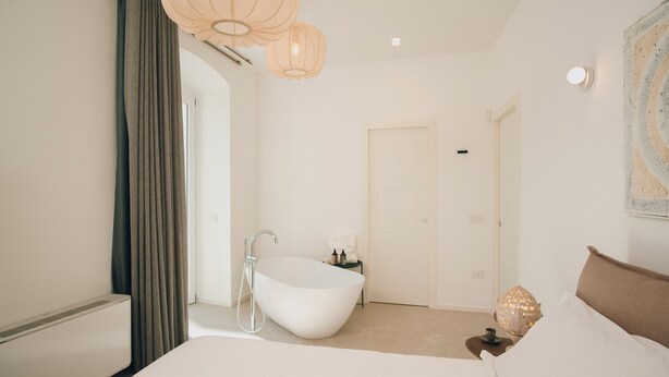 A modern bathroom with a freestanding bathtub, a shower, and a small table with toiletries. - Suite 13 B - San Lorenzo Suites (Putignano)