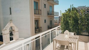 A balcony with a white railing, a table, and chairs. There is a bell in a stone structure on the left. - Suite 13 B - San Lorenzo Suites (Putignano)