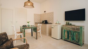 A compact kitchen with a dining area, a refrigerator, a television mounted on the wall, and a small cabinet. - Suite 13 B - San Lorenzo Suites (Putignano)