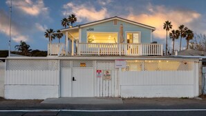 A light blue building with a balcony, a white fence, and palm trees in the background.