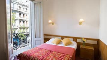 Habitación de hotel con una cama, dos lámparas de noche, una mesita de noche y un ventanal con vistas a edificios.
