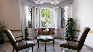 Ein Zimmer mit zwei Ledersesseln, einem kleinen runden Tisch mit Blumenvase und einem Fenster mit Vorhängen.