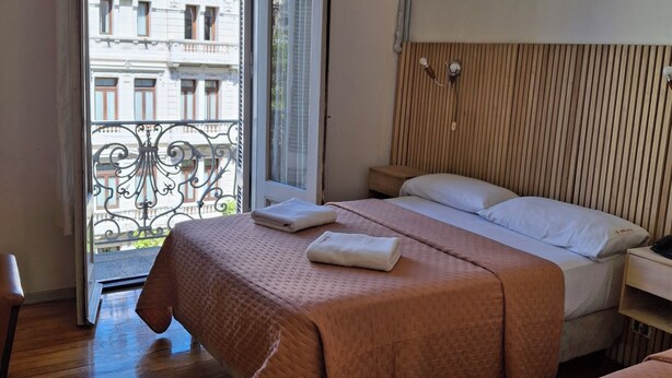 Ein Hotelzimmer mit zwei Betten, einem Holzkopfstück, einem Kronleuchter und einem Balkon mit Blick auf Gebäude.