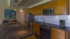 A kitchen with wooden cabinets, stainless steel appliances, and a granite countertop. - Waiohuli Beach Hale C212 (Kihei)