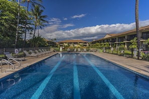 A swimming pool with lounge chairs and palm trees, surrounded by a building with a tiled roof.