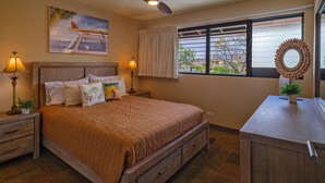 A bedroom with a bed, nightstands, a ceiling fan, a window with curtains, and a view of the outdoors. - Waiohuli Beach Hale C212 (Kihei)